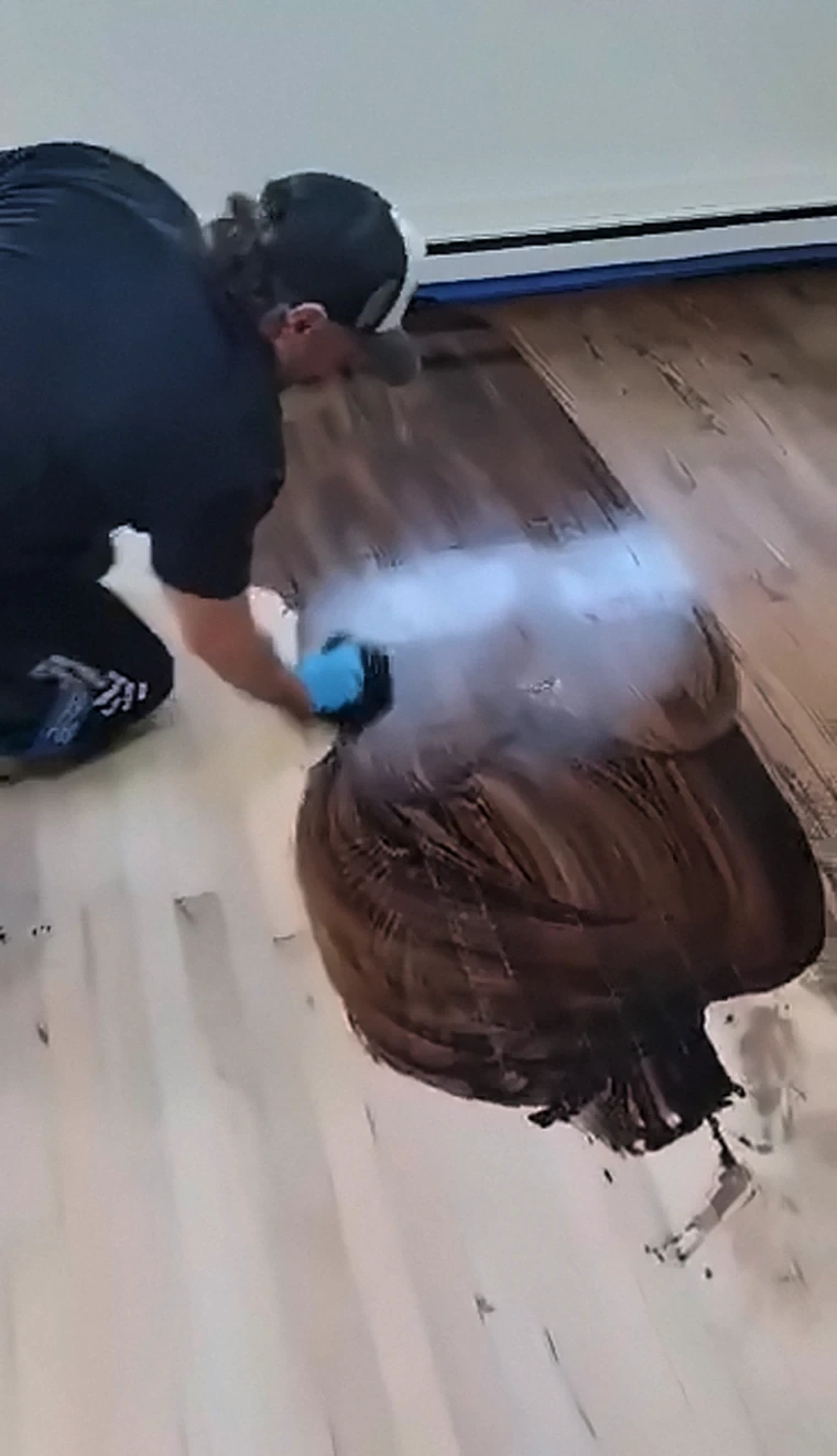 A rich, dark stain being hand-applied to a freshly sanded hardwood floor